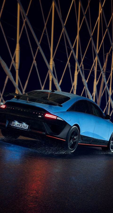 A Hyundai IONIQ 6 N drives across a bridge at night, surrounded by illuminated architectural elements.