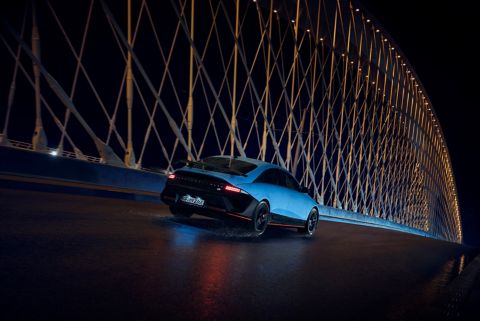 A Hyundai IONIQ 6 N drives across a bridge at night, surrounded by illuminated architectural elements.