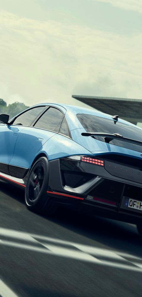 Hyundai i30 seen from rear three-quarter driving on a city street in front of modern buildings.