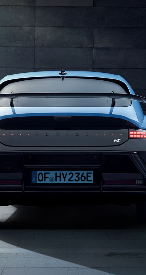 Rear view of a Hyundai IONIQ 6 N parked near a modern building with its driver-side door open.