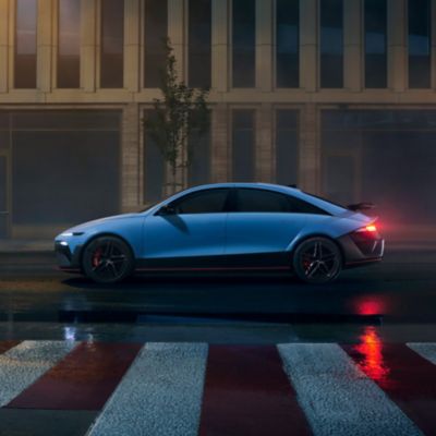 Side view of the Hyundai IONIQ 6 N parked in an urban area at night, reflecting city lights on wet pavement.