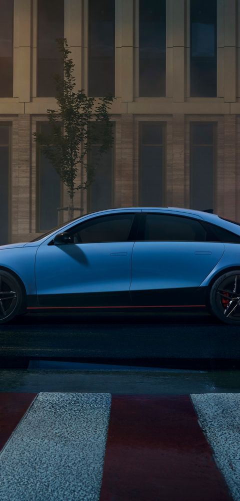 Side view of the Hyundai IONIQ 6 N parked in an urban area at night, reflecting city lights on wet pavement.