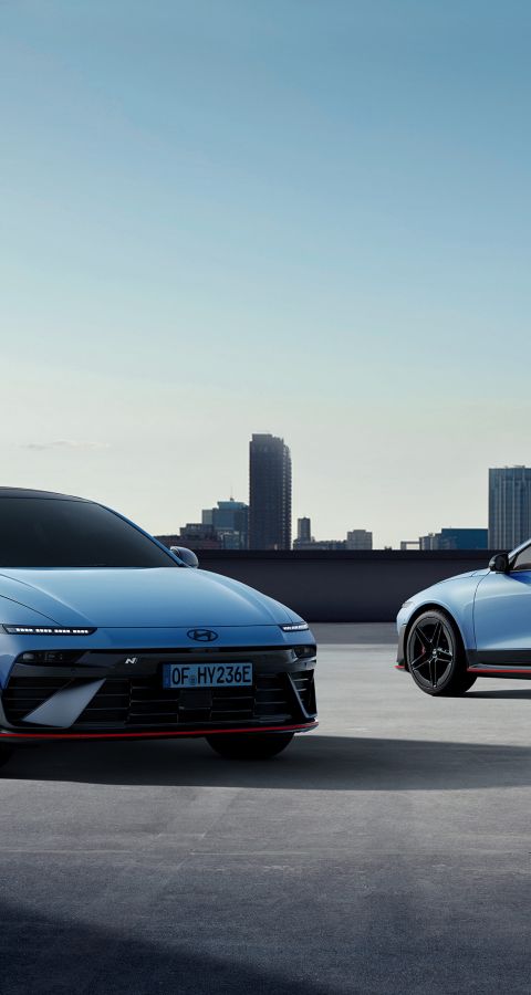 Two Hyundai IONIQ 6 N cars parked on a rooftop with a city skyline in the background.