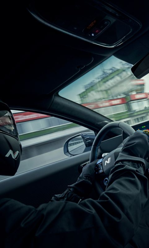 Driver wearing gloves navigates the IONIQ 6 N, showcasing the sporty cockpit and dashboard.
