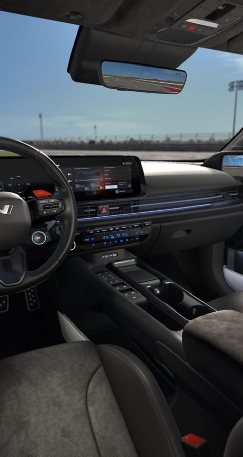 Interior view of Hyundai IONIQ 6N showing a driver-focused cockpit, dual displays and sporty seating on a race track.