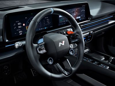 Close-up of the Hyundai IONIQ 6 N steering wheel with buttons and digital cluster displays in the background.
