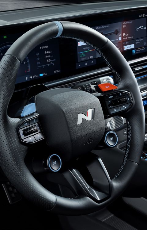 Detailní záběr na volant Hyundai IONIQ 6 N s tlačítky, v pozadí s digitálními přístrojovými displeji.