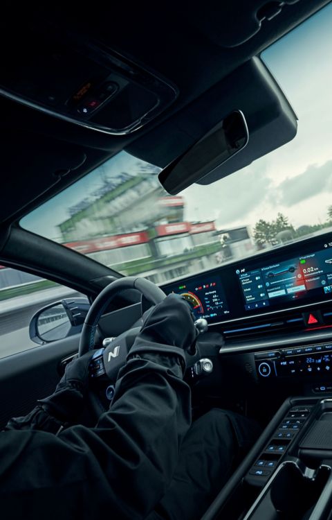 Sport driver operating Hyundai IONIQ 6 N high-performance EV with close-up of digital dashboard and interior cockpit