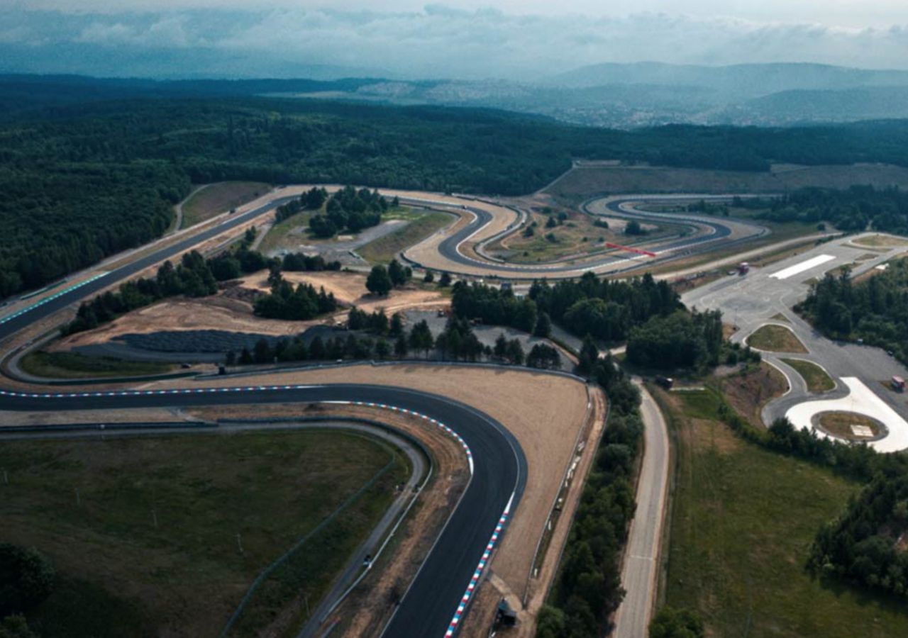 Aerial view of a winding racetrack surrounded by lush greenery, showcasing the layout and curves of the course.
