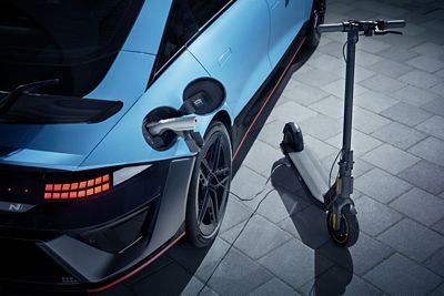 IONIQ 6 N charging an electric scooter via a cable on an outdoor paved surface.