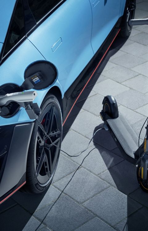 IONIQ 6 N nabíjející elektrickou koloběžku pomocí kabelu na venkovním zpevněném povrchu.