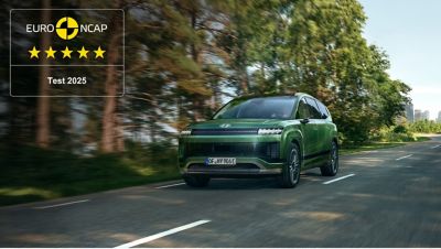 Hyundai IONIQ 9 van driekwart voor, rijdend op een weg met bomen op de achtergrond.