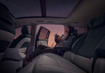Person with camera in back seat of Hyundai IONIQ 9, door open to a purple-pink sky.