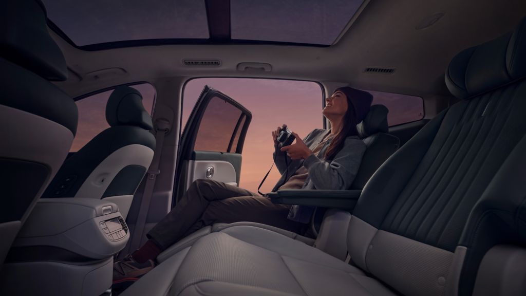 Persona con una cámara en el asiento trasero de un Hyundai IONIQ 9, con la puerta abierta a un cielo morado-rosado