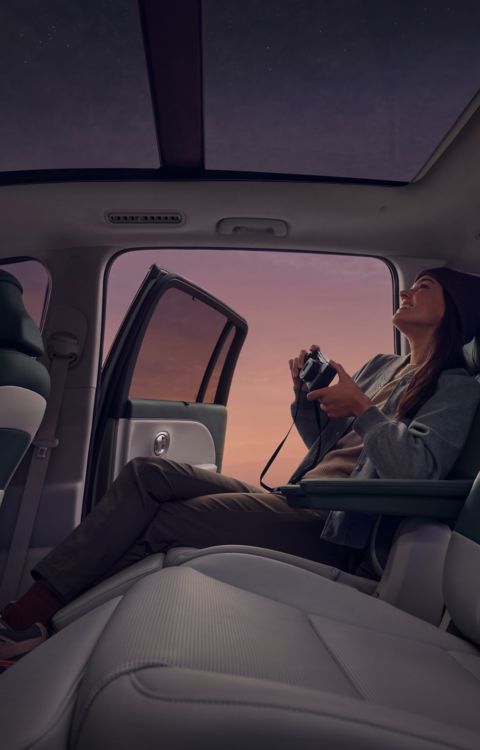Person with camera in back seat of Hyundai IONIQ 9, door open to a purple-pink sky.