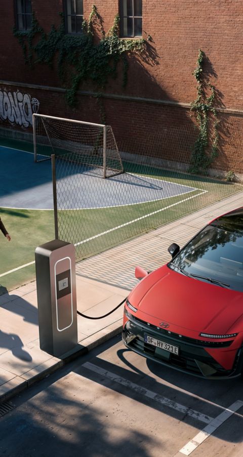 Hyundai IONIQ 3 charging on a city street with two people playing football next to it.