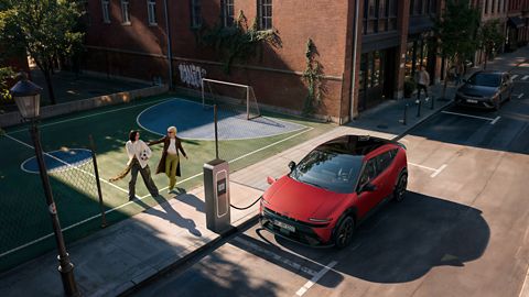 Ein Hyundai IONIQ 3 wird auf einer Straße in der Stadt aufgeladen, während daneben zwei Personen Fußball spielen.