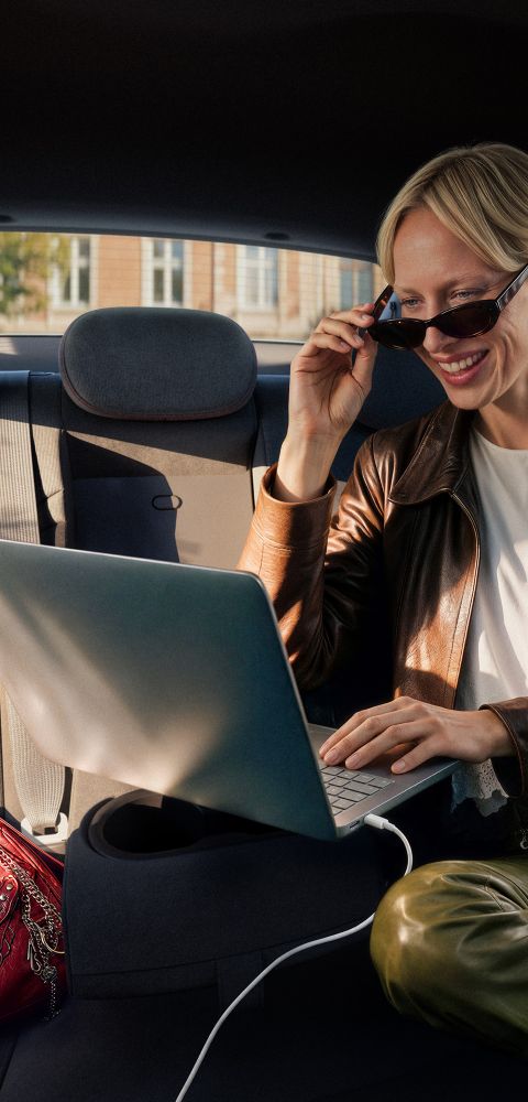 A woman typing on a plugged in laptop on the folded down middle rear seat inside the IONIQ 3.