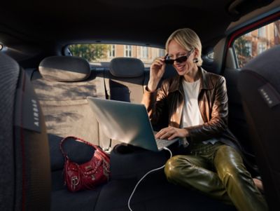 A woman typing on a plugged in laptop on the folded down middle rear seat inside the IONIQ 3.