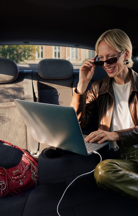 A woman typing on a plugged in laptop on the folded down middle rear seat inside the IONIQ 3.