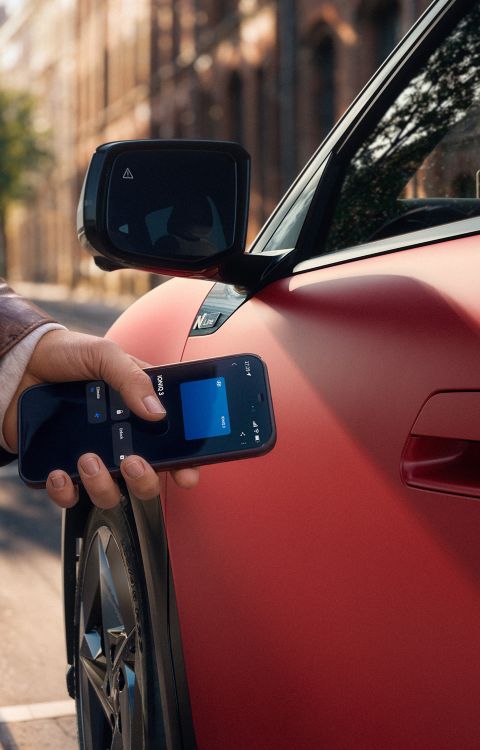 A hand holding a smartphone next to the door handle of the Hyundai IONIQ 3.