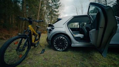 Une femme s'appuie sur une Hyundai IONIQ connectée à une station de recharge autonome publique.