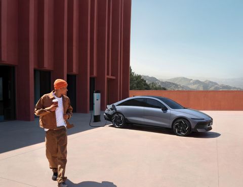 Hyundai IONIQ 6 charging at a station near a modern building while a person walks by