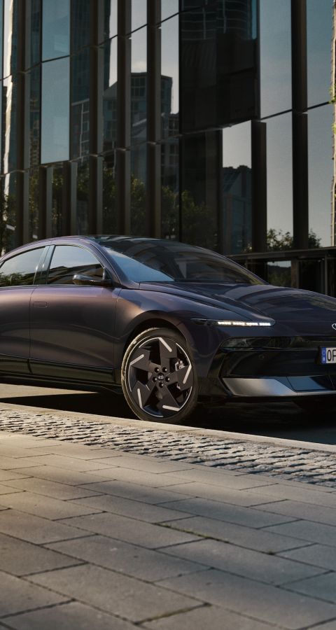 Hyundai IONIQ 6 electric sedan shown from the side parked on a city street with high rise buildings.