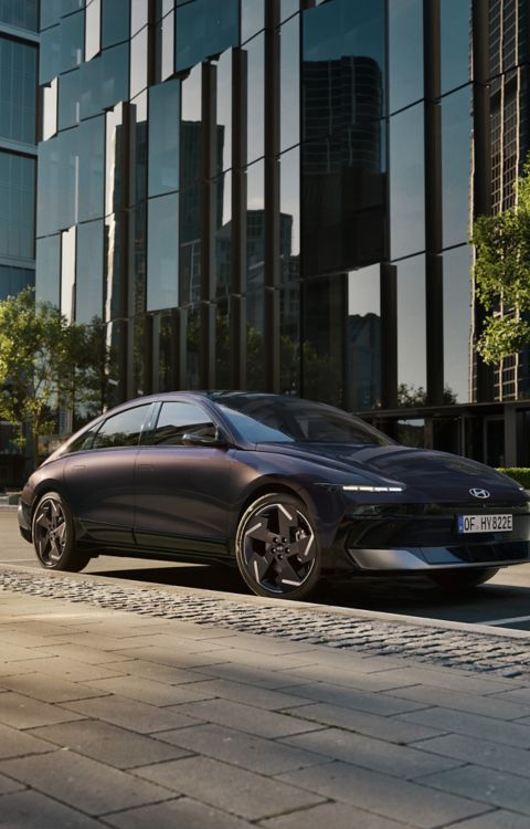 Hyundai IONIQ 6 electric sedan shown from the side parked on a city street with high rise buildings.