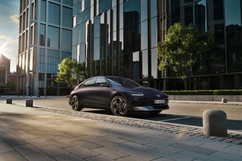 Hyundai IONIQ 6 electric sedan shown from the side parked on a city street with high rise buildings.