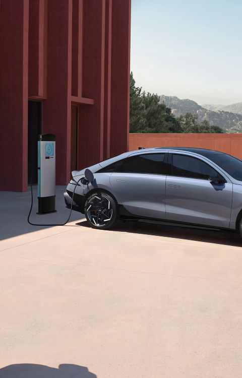 A man walking away from the Hyundai IONIQ 6 with a coffee cup while the car is plugged in to charge.
