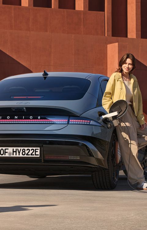 A woman leaning on IONIQ 6 charging an electric skateboard plugged into the external charging port.