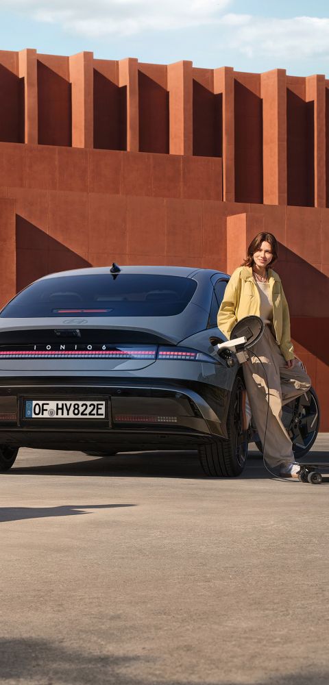 A woman leaning on side of the Hyundai IONIQ 6 electric sedan.