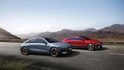 A grey IONIQ 6 and a red IONIQ 6 N Line driving next to each other on a highway with mountains in the background.