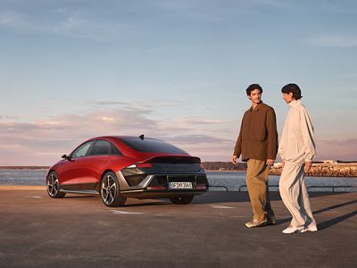 A man and woman walking past the rear of a Hyundai IONIQ 6 parked by the waterfront.