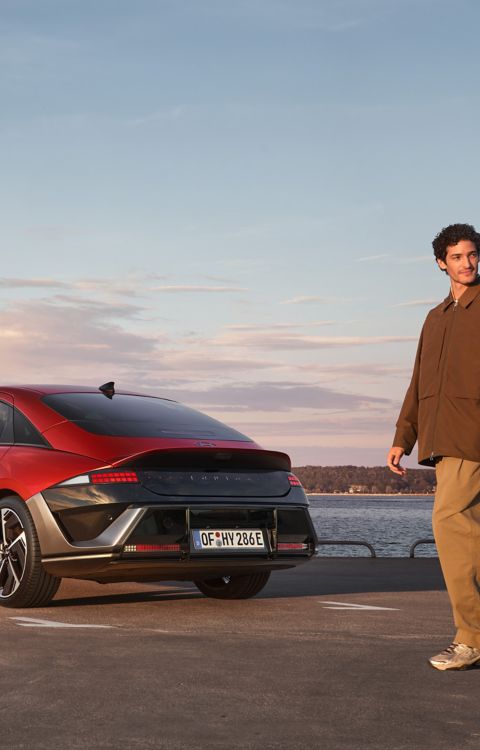 A man and woman walking past the rear of a Hyundai IONIQ 6 parked by the waterfront.