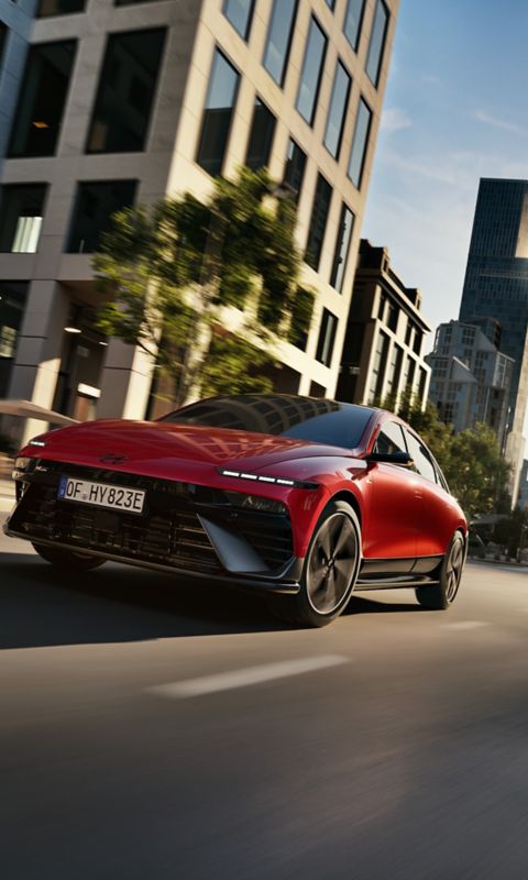  A red Hyundai IONIQ 6 N Line driving through a modern cityscape.