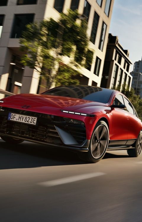  A red Hyundai IONIQ 6 N Line driving through a modern cityscape.