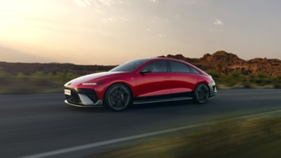The new Hyundai IONIQ 6 N Line in red driving down a highway with hills in the background. 