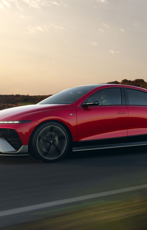 The new Hyundai IONIQ 6 N Line in red driving down a highway with hills in the background. 