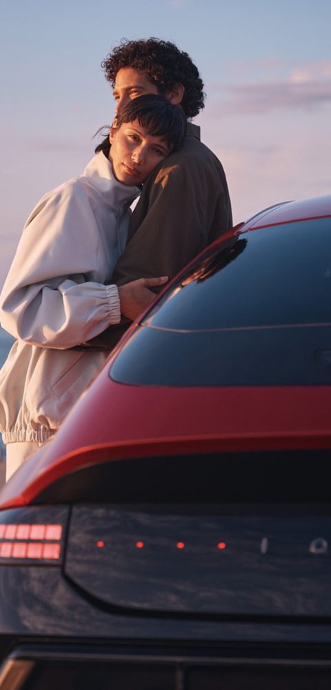 A man and a woman hugging while leaning on a Hyundai IONIQ 6 N Line parked next to the ocean.