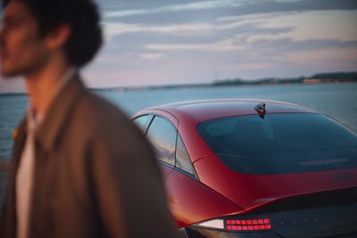 A man walking past a red Hyundai IONIQ 6 N Line parked next to the ocean.