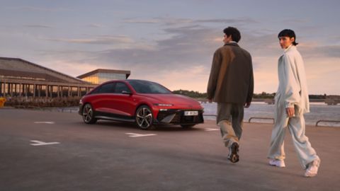 A grey IONIQ 6 and a red IONIQ 6 N Line driving next to each other on a highway with mountains in the background.	