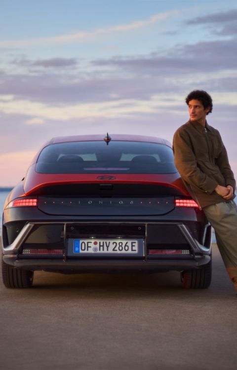 A man leaning on the side of a Hyundai IONIQ 6 N Line parked next to the ocean.