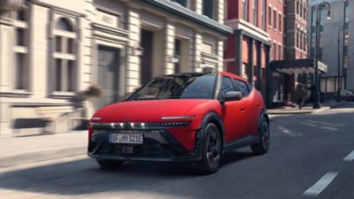Een rode Hyundai IONIQ 3 rijdt door een stadsstraat.
