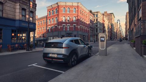 Hyundai IONIQ 3 parked and charging beside a city sidewalk.