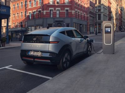 Hyundai IONIQ 3 parked and charging beside a city sidewalk.