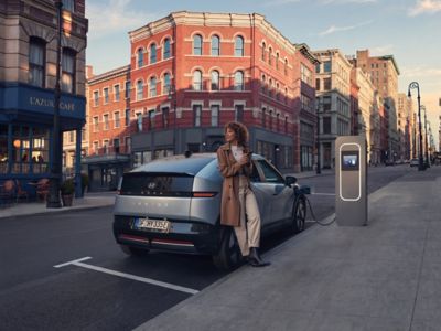 Person standing next to the Hyundai IONIQ 3 while charging in an urban setting.