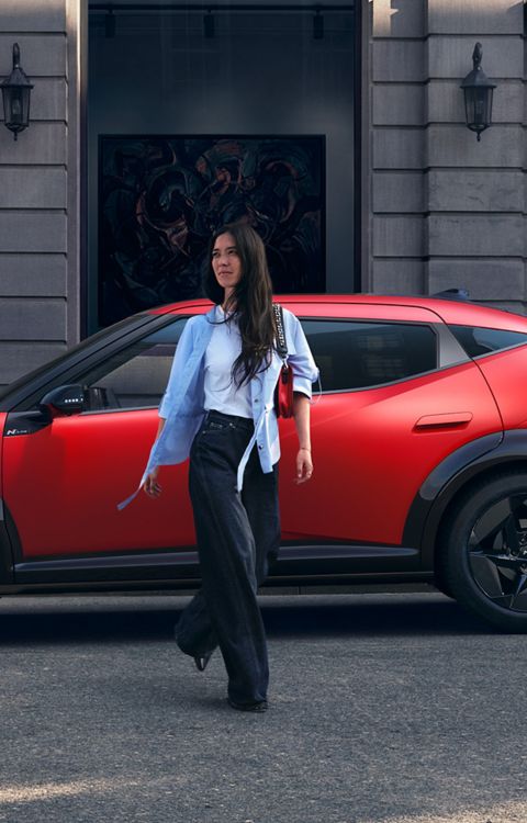 A woman walking away from the red Hyundai IONIQ 3 parked on the city street.