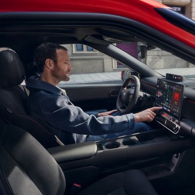 Het interieur van de Hyundai IONIQ 3, met een man zittend op de bestuurdersstoel die het PLEOS Connect-infotainmentsysteem bedient.